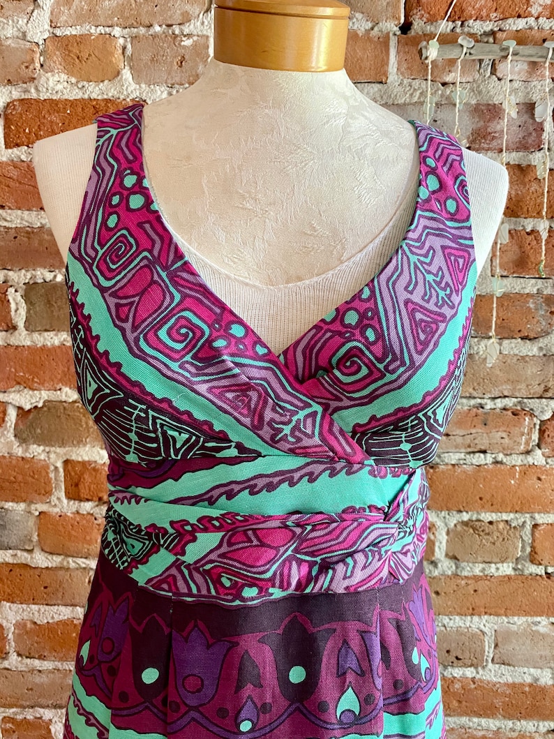 Peut inclure: Une robe sans manches avec un d&eacute;collet&eacute; en V et un motif g&eacute;om&eacute;trique color&eacute; dans les tons rose, violet, vert et noir. La robe a une ceinture &agrave; nouer &agrave; la taille et une jupe fluide.