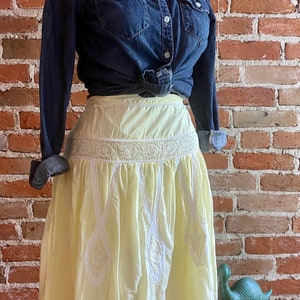 May include: A yellow cotton skirt with white eyelet lace trim. The skirt is gathered at the waist and has a scalloped hem.