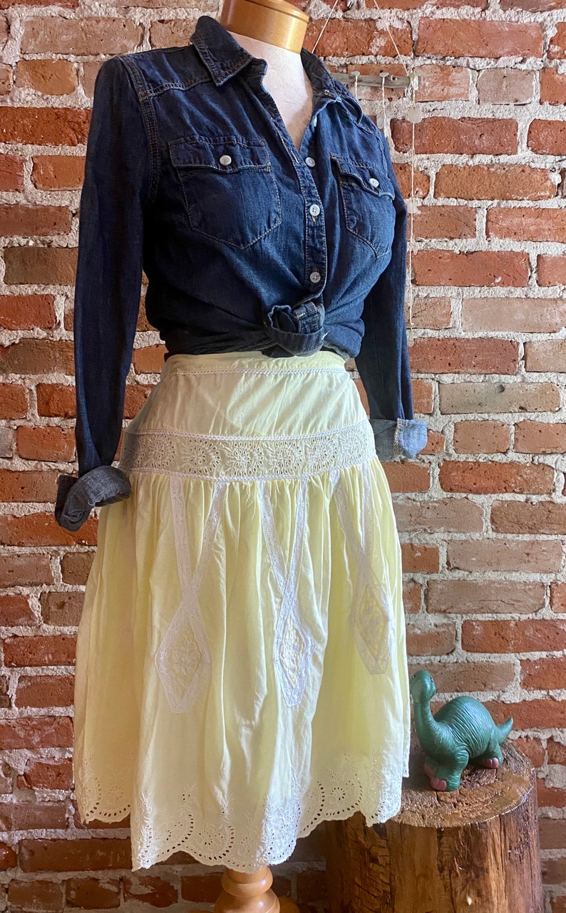 May include: A yellow cotton skirt with white eyelet lace trim. The skirt is gathered at the waist and has a scalloped hem.