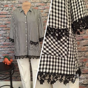 Può includere: Camicia a quadri bianchi e neri con bottoni e bordino in pizzo nero. La camicia ha una tasca sul lato sinistro e un colletto.