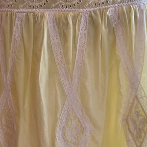 May include: A pale yellow cotton dress with white lace trim. The lace is in a diamond pattern and has a floral design.