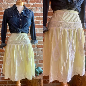May include: A yellow cotton skirt with white eyelet lace trim. The skirt has a gathered waist and a scalloped hem.