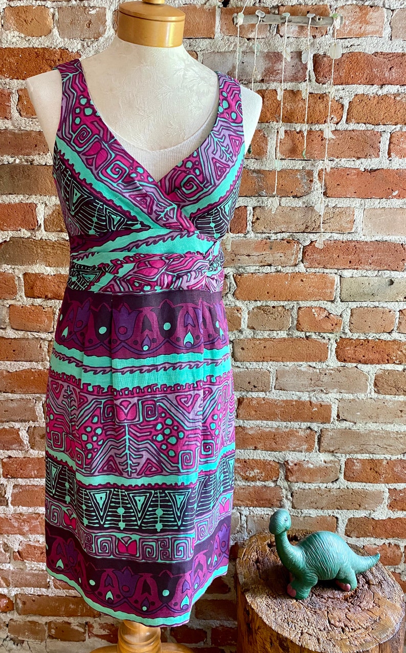 Peut inclure: Une robe sans manches avec un d&eacute;collet&eacute; en V et un motif g&eacute;om&eacute;trique color&eacute; dans des tons de violet, rose, vert et marron. La robe a un corsage ajust&eacute; et une jupe fluide.