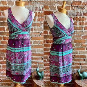 Peut inclure: Une robe sans manches avec un d&eacute;collet&eacute; en V et un motif g&eacute;om&eacute;trique dans les tons de violet, turquoise et noir. La robe a un corsage ajust&eacute; et une jupe fluide.