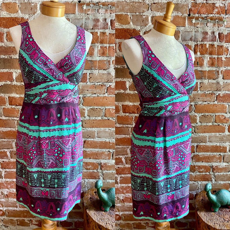 Peut inclure: Une robe sans manches avec un d&eacute;collet&eacute; en V et un motif g&eacute;om&eacute;trique dans les tons de violet, turquoise et noir. La robe a un corsage ajust&eacute; et une jupe fluide.
