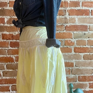 May include: A yellow cotton skirt with white eyelet lace trim. The skirt is gathered at the waist and has a flowing silhouette.