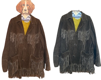 Puede incluir: Dos chaquetas de ante con flecos. Una es de color marrón intenso, la otra de color carbón oscuro. Ambas tienen un diseño clásico con botones, bolsillos y forro amarillo. Las chaquetas se exhiben en una percha con forma de perro.