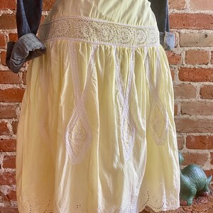 May include: A pale yellow cotton skirt with white eyelet lace trim. The skirt has a gathered waist and a full, flowing silhouette.