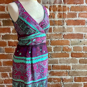 Peut inclure: Une robe sans manches avec un d&eacute;collet&eacute; en V et un motif g&eacute;om&eacute;trique color&eacute; dans des tons de rose, violet, turquoise et noir. La robe a un corsage ajust&eacute; et une jupe fluide.