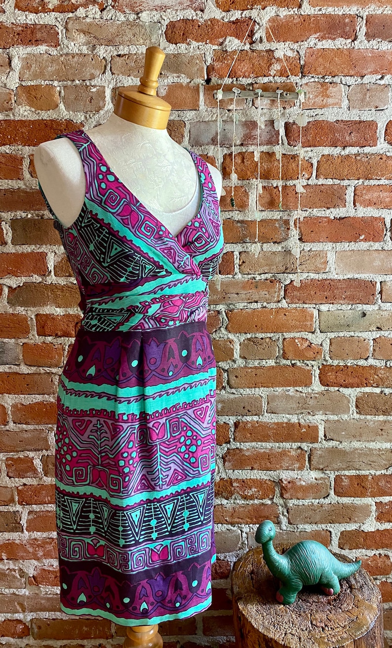 Peut inclure: Une robe sans manches avec un d&eacute;collet&eacute; en V et un motif g&eacute;om&eacute;trique color&eacute; dans des tons de rose, violet, turquoise et noir. La robe a un corsage ajust&eacute; et une jupe fluide.