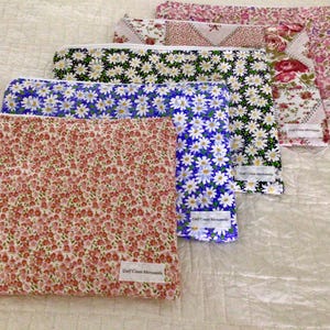 May include: A collection of floral print zippered pouches in various colors. The pouches feature patterns of daisies, small flowers, and roses. Each pouch has a white zipper and a small label that reads "Gulf Coast Mercantile".