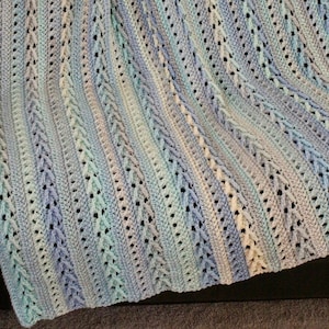 May include: A crocheted baby blanket in shades of blue, white, and gray with a textured, lacy pattern.