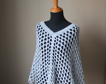 Puede incluir: Un poncho de crochet gris claro, de tejido abierto, con cuello en V, exhibido en un maniquí de madera. El poncho tiene un diseño suelto y aireado, perfecto para superponer. El color neutro lo hace versátil.