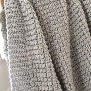 Puede incluir: Una manta de punto de ganchillo gris con un patrón de tejido de waffle.