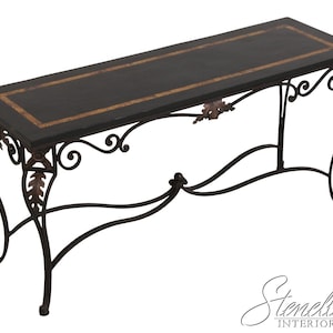 May include: A rectangular console table featuring a dark black top with a decorative brown border. The base is constructed from black metal with ornate scrollwork and bronze-colored leaf accents along the frame and legs.