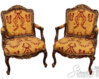 May include: Two antique armchairs with ornate, dark wood frames and gold accents. The seats and backs feature a yellow fabric with a repeating red floral pattern. The chairs have curved legs and armrests, showcasing a classic design.