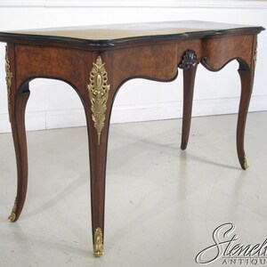 May include: A brown wooden writing desk with a black top and gold accents. The desk has a single drawer and curved legs.
