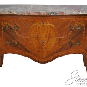 May include: A two-drawer chest with a marble top and intricate marquetry details. The chest is made of wood and has a curved front and legs. The chest is decorated with brass hardware and has a light brown finish.