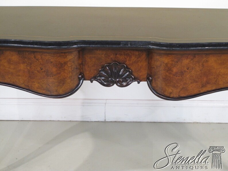 May include: A wooden console table with a dark brown finish and a curved top. The table has a black and gold trim and a carved detail on the front.