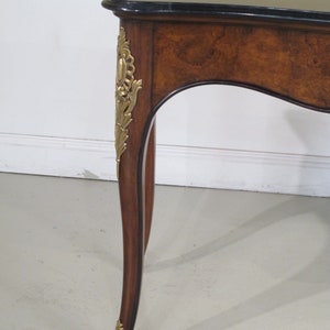 May include: A brown wooden table with a black marble top and gold accents. The table has a curved leg design and intricate details.