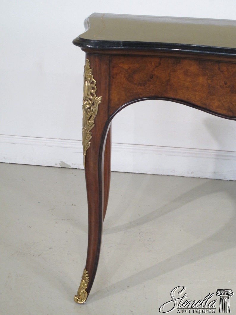May include: A brown wooden table with a black marble top and gold accents. The table has a curved leg design and intricate details.