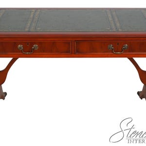 May include: A rectangular wooden desk with a rich reddish-brown finish, featuring a dark green leather inlay on the top surface with gold-toned decorative border detailing. The desk includes two front drawers with brass-colored metal pull handles.