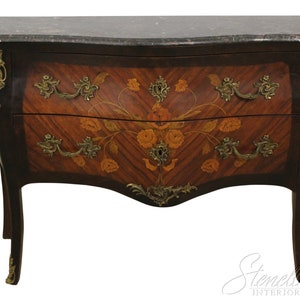 May include: A two-drawer antique chest with a dark marble top and curved front. The chest features a floral marquetry design on the drawer fronts, brass hardware, and dark wood legs. The chest is a classic piece of furniture.