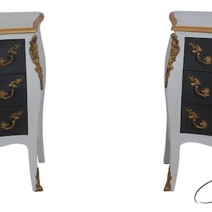 May include: Two matching white and black bedside tables with three drawers each. The tables have gold accents on the edges, drawer pulls, and decorative trim. The legs are curved, and the overall style is ornate.