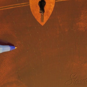 Pu&ograve; includere: Primo piano di una superficie in legno marrone con un buco della serratura e lievi graffi. Una penna blu &egrave; appoggiata sulla superficie.