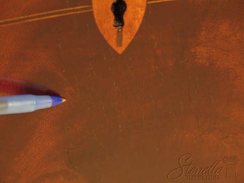 Pu&ograve; includere: Primo piano di una superficie in legno marrone con un buco della serratura e lievi graffi. Una penna blu &egrave; appoggiata sulla superficie.