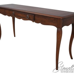 May include: A long, dark brown wooden console table with a single drawer and ornate, curved legs. The table features a scalloped apron and decorative drawer pulls. The top has a rectangular shape with a slightly raised edge.