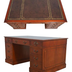 May include: A large, wooden desk with a brown leather top and multiple drawers. The desk has a rectangular shape with a dark brown leather surface, accented with gold trim. The desk has several drawers on both sides and ornate brass handles.