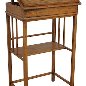 May include: A wooden antique writing desk with a slanted top, a small shelf, and a lower shelf. The desk is made of light brown wood and has a classic design. The desk is approximately 30 inches tall.
