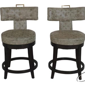 May include: Four bar stools with dark wooden legs and a circular footrest. The seats and backs are upholstered in a patterned fabric. Each stool has a small, gold-colored handle on the back.
