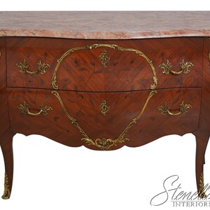 May include: A mahogany-colored chest of drawers with a marble top. The chest features two drawers with ornate brass handles and decorative trim. The curved design and cabriole legs add to its antique aesthetic. The chest is a classic piece of furniture.
