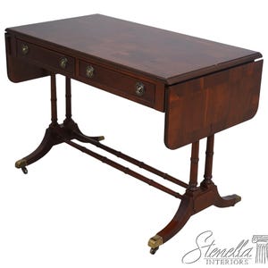 May include: A dark brown wooden drop-leaf table with two drawers and brass hardware. The table has a rectangular top and is supported by four legs with brass casters. The table's leaves are folded down.