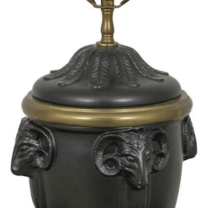 May include: A black and gold table lamp with a ram's head design. The lamp has a round base and a tall, slender neck. The shade is made of black metal and has a decorative design.
