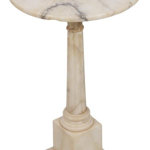 May include: A round pedestal table crafted from cream-colored stone with natural veining. The table features a circular top supported by a slender, tapered column that rests on a square base. The surface displays subtle grey and brown marble patterns.
