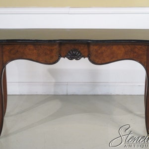 May include: A brown wooden console table with a black marble top and gold accents. The table has a curved front and legs, and features a decorative carved design on the front.