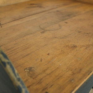 Op de afbeelding: Een houten dienblad met een blauw geverfd frame. Het dienblad heeft een versleten, rustieke uitstraling en is gemaakt van natuurlijk hout.