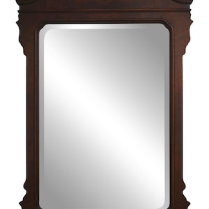 May include: A dark brown, rectangular wall mirror with an ornate, carved wooden frame. The frame features a decorative top with a central finial and curved accents. The mirror's surface is reflective, and the overall design is traditional.