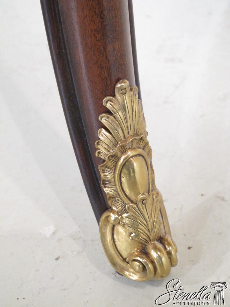 May include: Close-up of a wooden table leg with a gold metal decorative foot. The foot features a stylized floral design.