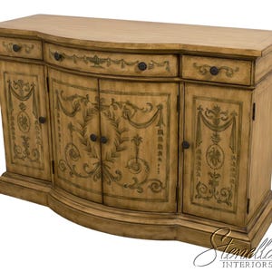 May include: A light brown wooden sideboard with a curved front and decorative floral designs. The cabinet has two drawers and three doors with black hardware. The piece is a classic furniture item.