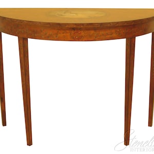 May include: A half-moon shaped wooden console table with four slender legs. The table has a light brown finish with decorative floral accents along the edge and a painted oval design on the tabletop. The legs are tapered and have a similar finish.