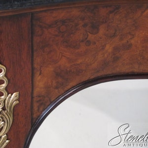 May include: Close-up of a wooden table with a dark brown finish and intricate brass accents. The table has a curved edge and a black marble top.