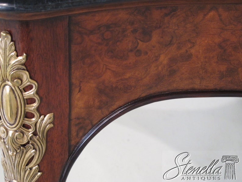May include: Close-up of a wooden table with a dark brown finish and intricate brass accents. The table has a curved edge and a black marble top.