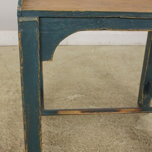 Op de afbeelding: Een vintage houten tafel met een donkerblauwe geverfde afwerking. De tafel heeft een eenvoudig ontwerp met een rechthoekig blad en twee poten aan elke kant. De tafel is verweerd en vertoont tekenen van slijtage, wat bijdraagt aan zijn rustieke charme.