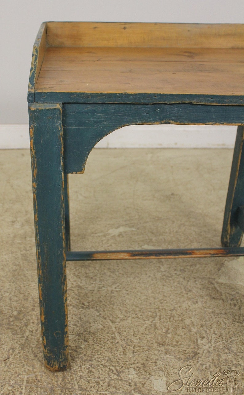 Op de afbeelding: Een vintage houten tafel met een donkerblauwe geverfde afwerking. De tafel heeft een eenvoudig ontwerp met een rechthoekig blad en twee poten aan elke kant. De tafel is verweerd en vertoont tekenen van slijtage, wat bijdraagt aan zijn rustieke charme.