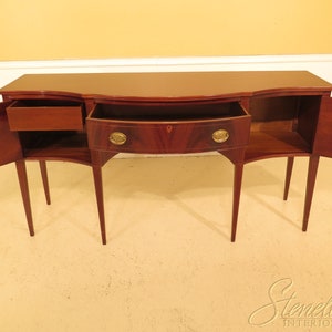 Pu&ograve; includere: Un credenza in legno di mogano con tre cassetti e due ante. Le ante sono aperte, rivelando gli scaffali interni. La credenza ha un fronte curvo e quattro gambe.