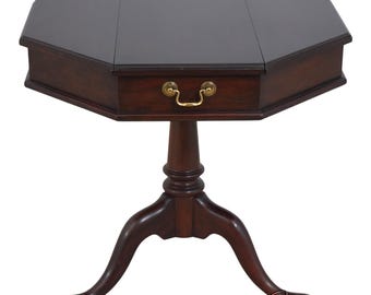 May include: A dark brown wooden pedestal table with an octagonal top and a single drawer featuring a brass pull handle. The table is supported by a central column that branches into three curved legs with rounded feet on a white background.